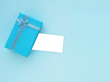 Blue gift box with bow and empty white card on blue background. Top view, flat lay with copy space. Festive background concept.の写真素材
