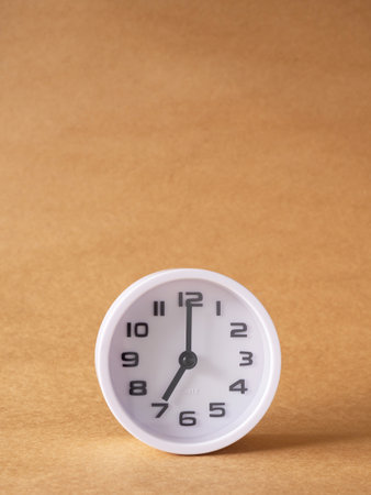 Vertical close up, white clock shows time at 7 o'clock on the office brown workplace tabletop. Copy space for your text. Business and education concept.の写真素材