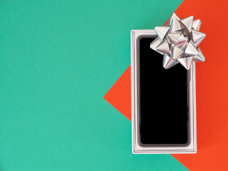 Festival gift-giving concept, New mobile phone in box with silver bow on red-green paper background.の写真素材