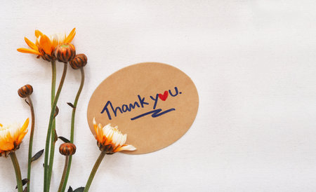 Top view flat lay, The word "thank you" message on brwon oval card  with orange chrysanthemum blooming on rustic wooden background.の写真素材