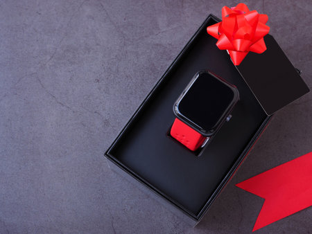 Smartwatch in the black gift box tied with a red bow and black greeting cards on dark grey background. Top view, flat lay with copy space. The concept for the season of giving.の写真素材
