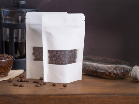 Roasted coffee beans in white transparent window paper bag with zipper and  bowl, glass bottle, coffee pot on wooden background. Space for your text.の写真素材