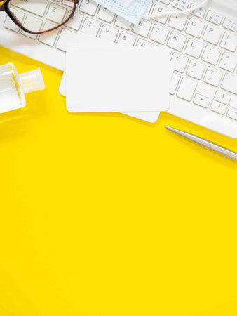 Flat lay, white business card over the keyboard with pen, hand sanitizer alcohol gel on a yellow workplace table. Top view with space for text. Business and education concept.の写真素材