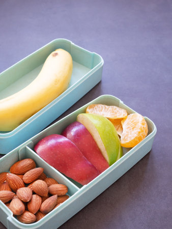 Fresh fruit in light green lunch box with almond, apple, orange, banana on grey background. Take away food. copy space, healthy eating concepts.の写真素材