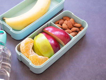 Fresh fruit in light green lunch box with almond, apple, orange, banana, water bottle on grey background. Take away food. copy space, healthy eating concepts.の写真素材