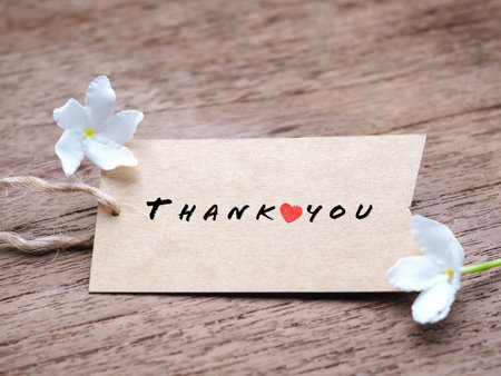 The word "Thank you" and small red heart on the brown tag and white flower on rustic wooden background.の写真素材