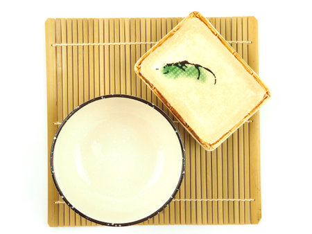 Top view, empty beige ceramic bowl and small plate on bamboo mat isolated on a white background. Use for home or restaurant, food design. Kitchen accessory. Japanese styleの写真素材