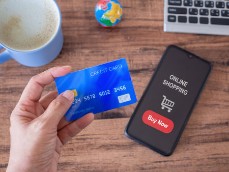 Hand-holding credit card and smartphone show screen online buy now on the table. Online shopping,...
