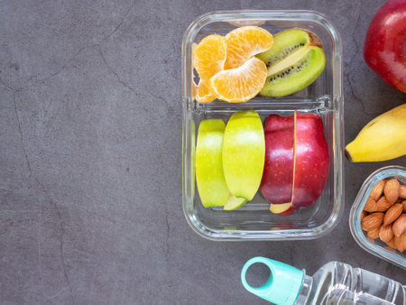 Top view, Glass container lunch box fresh fruit with apple, kiwi, banana, orange, almond and water bottle on grey background. Take away food, blank space for text. Healthy eating concepts.の写真素材