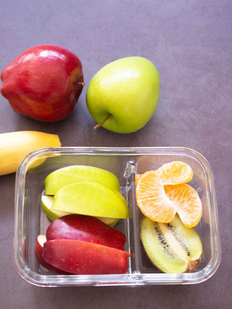 Glass container lunch box of mix fruit (apple, kiwi, orange) and banana on grey background. Take away food. copy space, healthy eating concepts.の写真素材