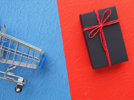 Black gift box tied with red rope and shopping cart on red and blue background, online shopping concept.の写真素材