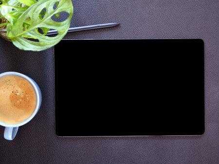 Top view, flat lay mock up digital tablet pc computer with blank black screen and wireless pen, coffee cup, little tree on black office table.の写真素材