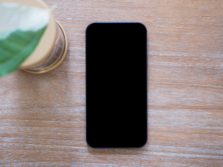 Top view, blank black screen of smartphone and little tree on wooden background. Template, mock-up empty screen of mobile phone for text and logo of product.の写真素材