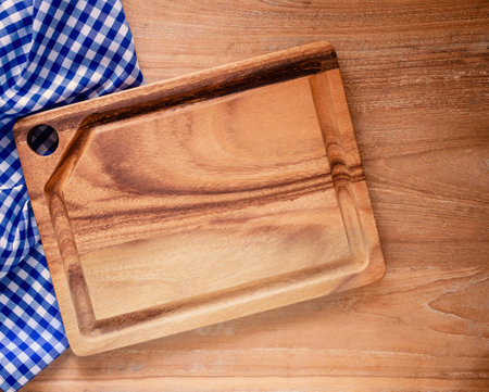 Empty cutting board on blue and white checkered fabric or napkin on rustic wood background. Concept kitchen utensils and tableware. Mock-up, for food product. Top view, flat lay with copy space.の写真素材