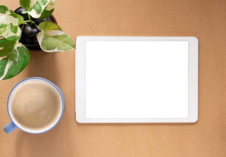 Blank screen of tablet and coffee cup with plant on brwon workplace. Top view, flat lay with copy space. Template for business and education.の写真素材