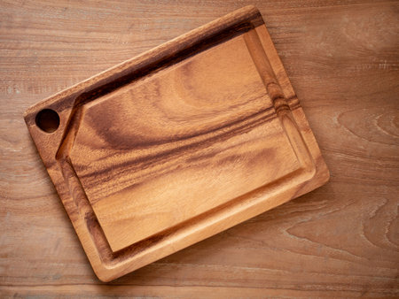Empty wooden cutting board over rustic wood background. Mock up, template for food product. Top view, flat lay with copy space. Concept kitchen utensils and tableware.の写真素材