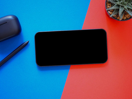 Top view, blank black screen of smartphone and wireless earphone in- charging case, pen on blue-red background. Template, mock-up empty screen of mobile phone for text and logo of product.の写真素材