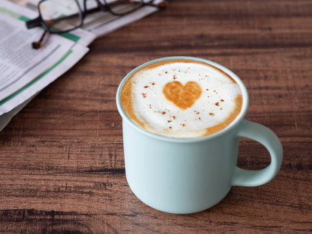 Hot latte coffee with art heart shape in light green ceramic mug on brown wooden table.の写真素材