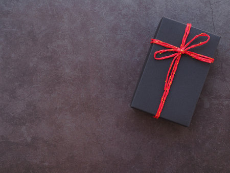 Black gift box tie red rope on dark grey background. Holiday season concept. Top view, flat lay with copy space.の写真素材