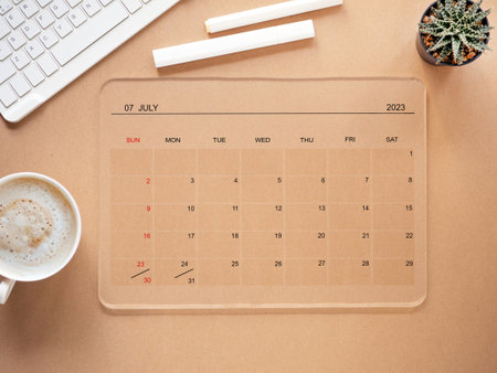 The online calendar app on a tablet computer shows the screen in July 2023, on a brown background and coffee cup, and cactus. Reminder with the calendar application for schedule planning.の写真素材