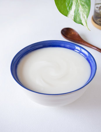 Homemade greek yogurt or sour cream in blue bowl with wooden spoon over white wooden background. Food helps the digestive system.の写真素材