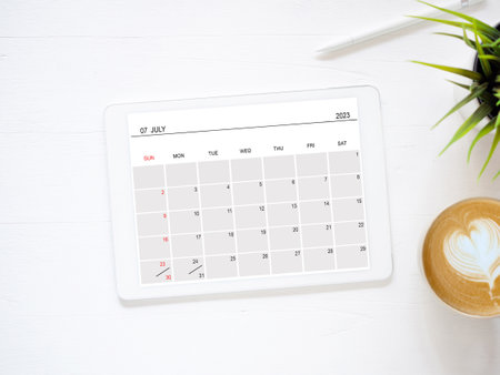 Tablet computer with an open app of the calendar for July 2023 year and a cup of coffee on white background for setting weekly, and monthly goals to achieve the goals set. Concept schedule planningの写真素材