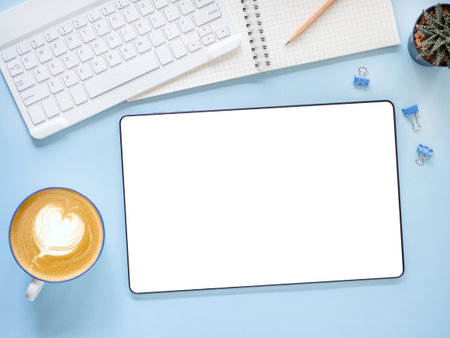 Blank screen of tablet and coffee cup, cactus, nootebook, pencil, keyboard on blue workplace. Top view, flat lay with copy space. Template for business and education.の写真素材