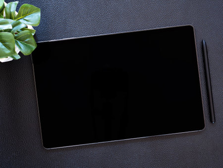 Top view. flat lay digital tablet pc computer with blank black screen and wireless pen, little tree on black leather background.の写真素材