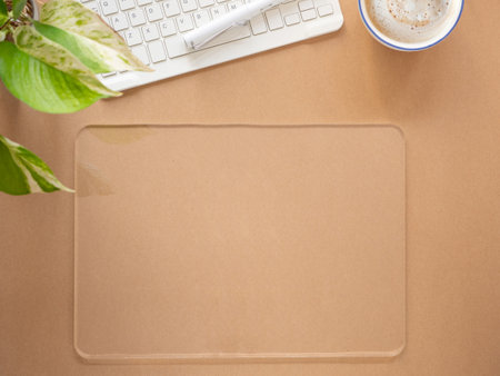 Transparent blank screen of tablet and coffee cup, keyboard with plant on brown workplace. Top view,...