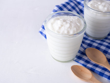 Greek yogurt in cup glass and checkered blue cloth, wooden spoon on white wooden background.の写真素材