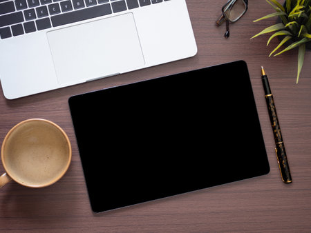 Mock-up tablet with blank screen, laptop, coffee, pen, and house plant on brown table. Copy space for advertising of products, text, and design. Business and education concept. Top view, flat lay.の写真素材