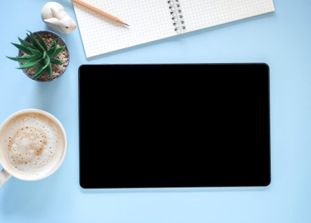 Blank screen of tablet and coffee cup, cactus, nootebook on blue workplace. Top view, flat lay with copy space. Template for business and education.の写真素材