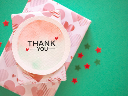 Top view, The word "thank you" message on watercolor paper with gift box and star shape over green paper background.の写真素材