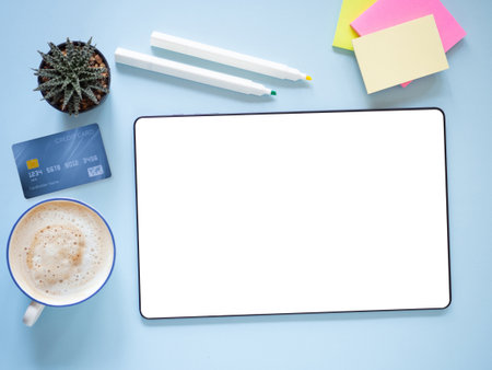 White screen mock-up digital tablet with coffee cup, credit card, cactus and office supplies on blue...