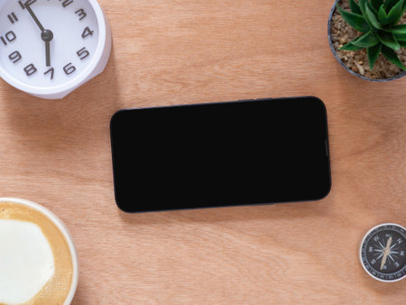 Blank mobile phone black screen isolated for mockup. coffee cup, cactus, clock on wooden workplace....