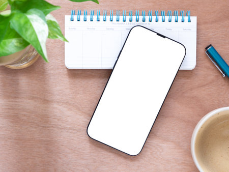 Mobile telephone empty display mock-up with coffee cup and plant, notebook, pen on  wooden background. Top view composition. Concept online shopping, blog, logo, product, and social media.の写真素材