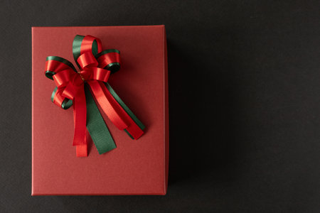 Top view, flat lay of red gift box with red and green bow over black background. Concept for holiday.の写真素材