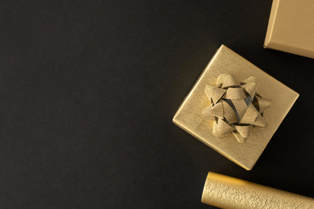 Golden gift box with gold bow on black background and gold gift wrapping paper. Top view, flat lay with copy space. Concept for holiday.の写真素材