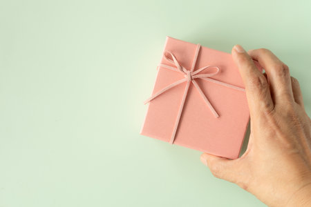 Hand of pink gift box over green background. Top view, flat lay with copy space. Concept for happy birthday, thank you, congratulations, Mother's day, anniversary, Valentine's day.の写真素材
