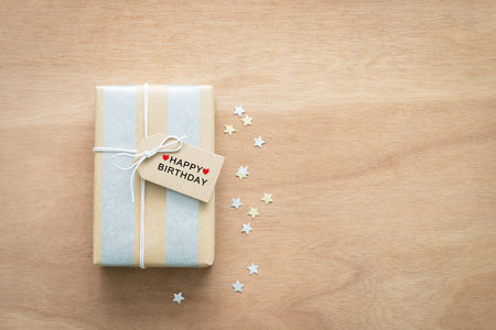 Top view, Gift box with brown tag with the words Happy birthday surrounded by silver and gold paper stars on a wooden background. Concept ideas for writing birthday wishes.の写真素材