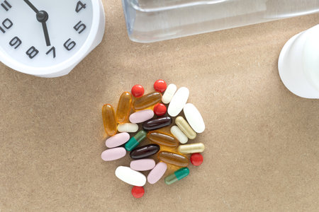 Top view of pile of dietary supplement pills, clock, water bottle on brown background. Healthcare, supplement, daily concept.の写真素材