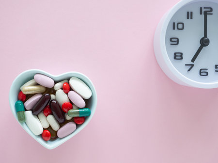 Top view, flat lay a light blue, a heart-shaped bowl filled with various pills and capsules and clock on pink background. Health care, pharmacology and minimal medical concept.の写真素材