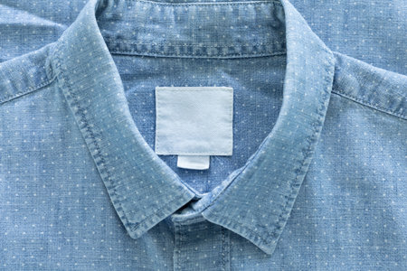 A close-up of a light blue, polka-dotted shirt, focusing on the collar with a blank white label, a button on the placket, and a portion of the sleeve.の写真素材