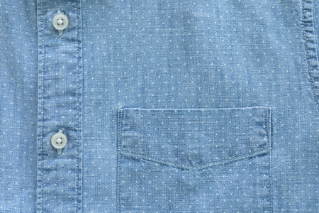 A close-up shot of a light blue shirt featuring a subtle white polka dot pattern, a chest pocket, and a button-down placket with two visible buttons.の写真素材