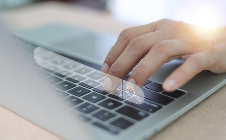 A close-up shot of a person's hand typing on a laptop keyboard, with a prominent, superimposed search bar icon. Searching browsing Internet global data information data online search from internet.の写真素材