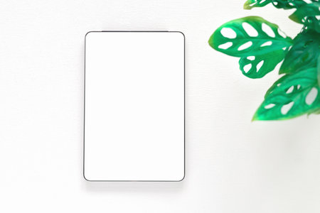 Template, mockup of digital tablet with a blank white screen and plant  over a white wooden background. Concept online shopping, blog, logo, product, and social media. Top view with copy space.の写真素材