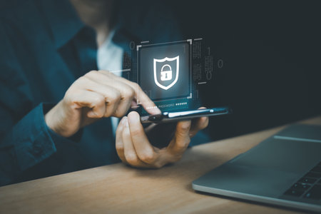 Close-up of hands holding a smartphone, with a glowing security shield and padlock icon overlaid. Data privacy, and online protection against cyber threats. Digital security concept.の写真素材