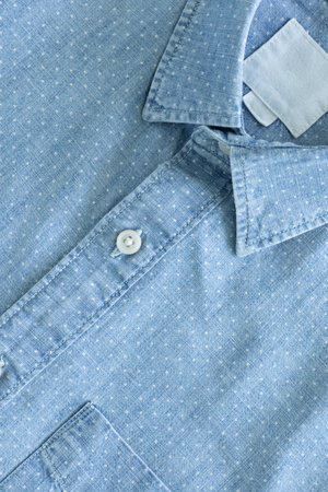 A close-up of a light blue, polka-dotted shirt, focusing on the collar with a blank white label, a button on the placket, and a portion of the sleeve.の写真素材