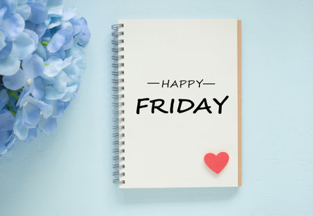Top view of an open spiral-bound notebook displaying  "HAPPY FRIDAY" on center with red heart and a blue hydrangea on blue wooden background. Concept of relaxation, the anticipation of the weekend.の写真素材