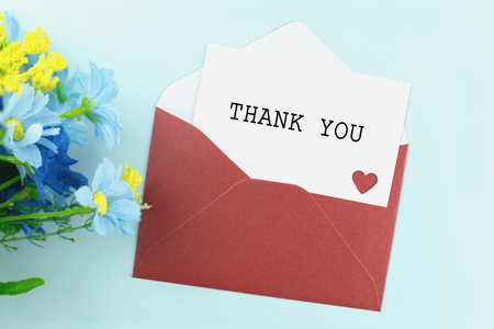 A thank you card is in a red envelope next to a bouquet of blue and yellow flowers on a light blue background. Concepts for showing gratitude, appreciation, and special messages on various occasions.の写真素材